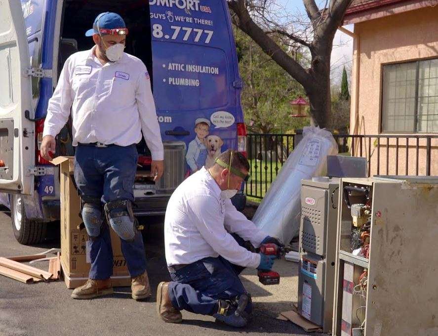 Home Comfort technicians working on HVAC equipment beside a service van