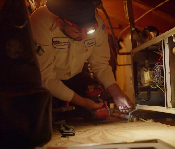 A tech repairing an AC unit in an attic