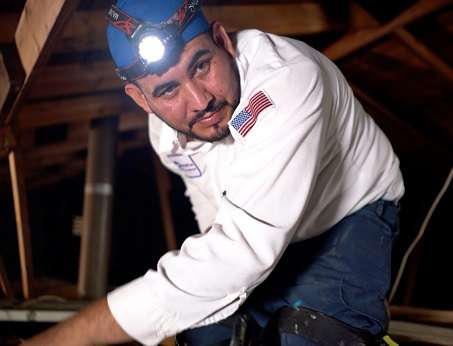 An AC technician working in an attic