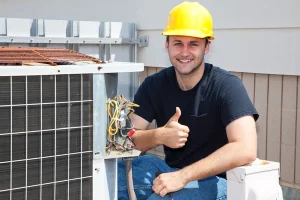 hvac tech by an hvac wearing a yellow hard hat with a thumbs up
