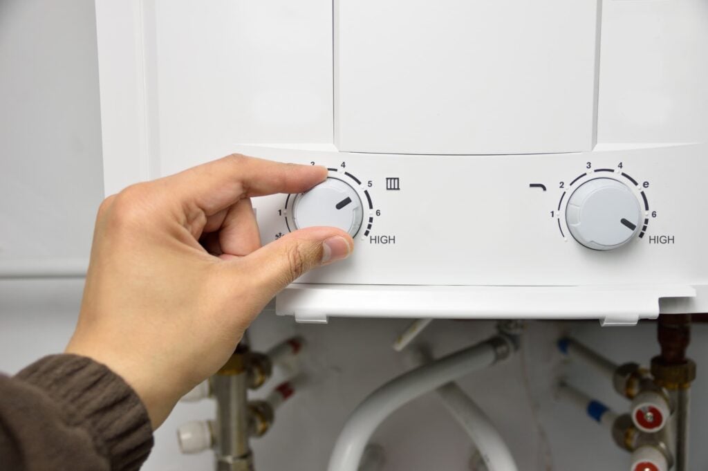 technician hand reaching up to turn a knob on a tankless water heater